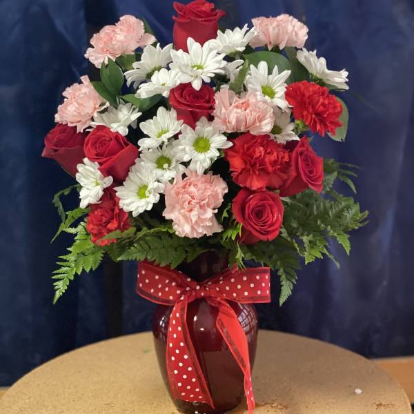 Red roses, white daisies, and pink carnations in a vase with a red polka-dot ribbon.