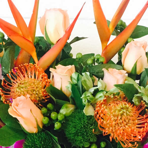 Tropical bouquet with orange heliconia, peach roses, and orange pincushion blooms
