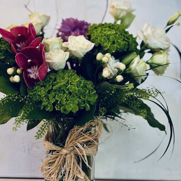 Bouquet of white roses, green hydrangeas, and magenta orchids in a glass vase