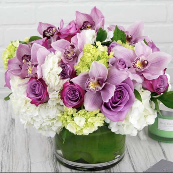 Pink orchids and roses arranged in a green glass vase