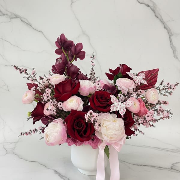 Bouquet of red and pink flowers in a white vase with a pink ribbon
