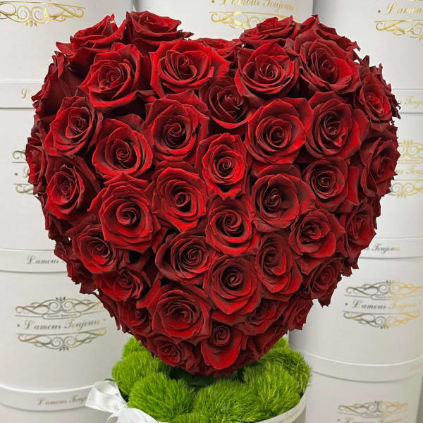 Heart-shaped arrangement of red roses in a round box with green moss and a white ribbon