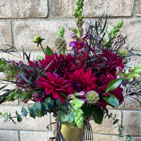 Magenta dahlias in a gold vase with dark foliage and green accents