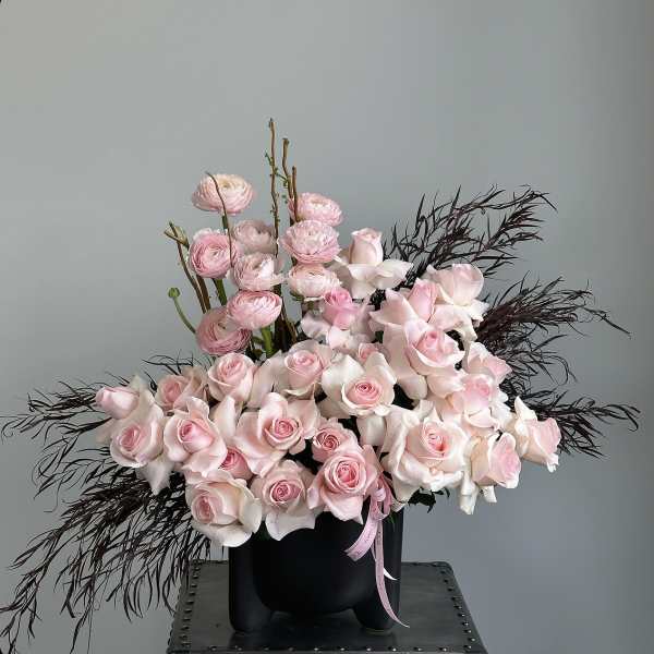 Pink roses and ranunculus in a black vase with dark feathery accents