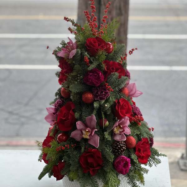 Christmas tree-shaped floral arrangement with red roses and pink orchids in a white pot