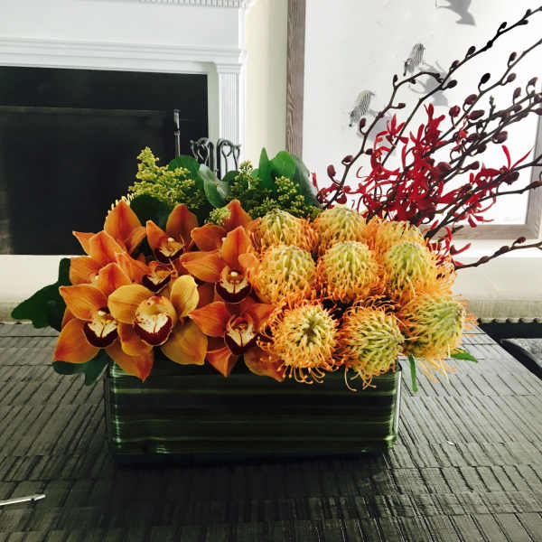 Orange orchids and yellow pincushion blooms in a rectangular vase