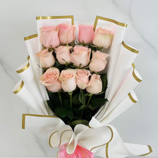 Hand-tied bouquet of light pink roses wrapped in sculpted white paper with gold trim