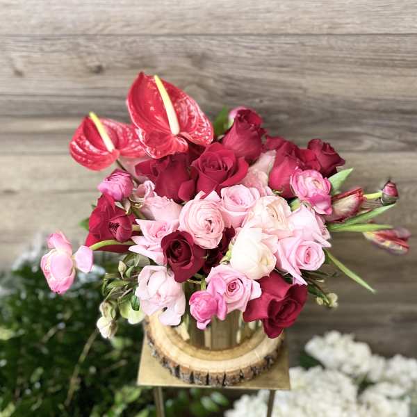 Pink and red roses with red anthuriums arranged in a wooden container