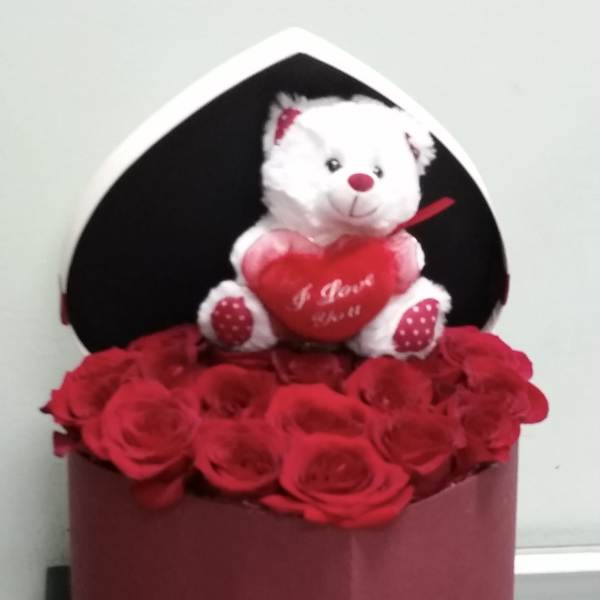 Red roses in a heart-shaped box with a white teddy bear holding a heart