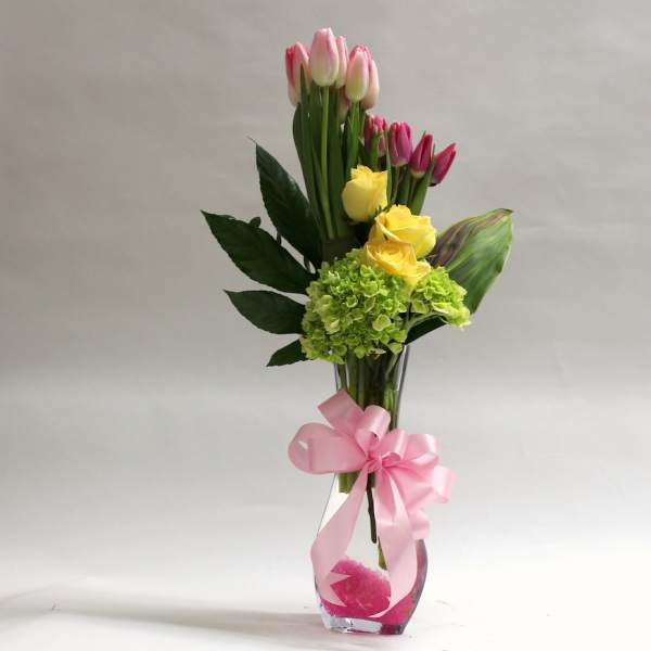 Pink and yellow tulips with green hydrangea in a glass vase with a pink ribbon