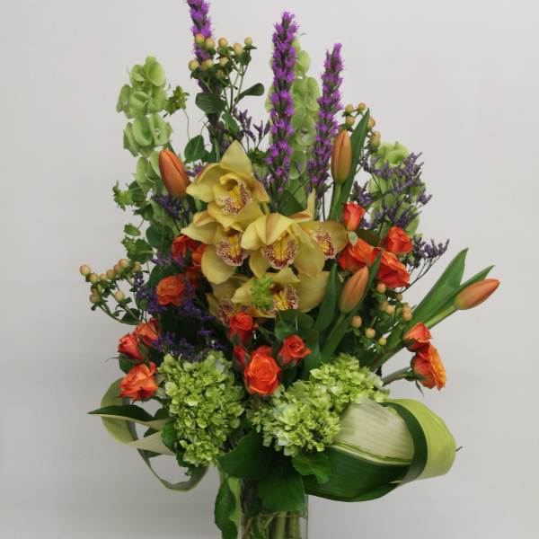 Tall mixed bouquet in a clear glass vase with yellow orchids and orange tulips