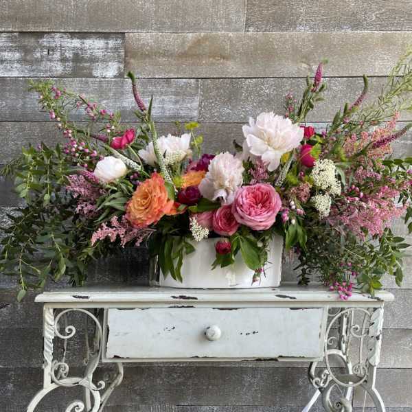 Large mixed floral arrangement in a white container on a small table