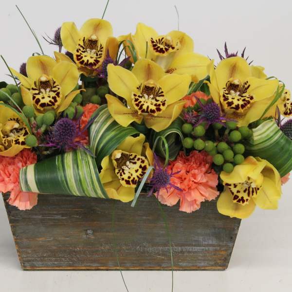 Yellow orchids and pink carnations in a rustic wooden planter