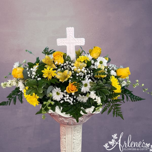Yellow roses and white daisies in a pedestal vase with a white cross centerpiece