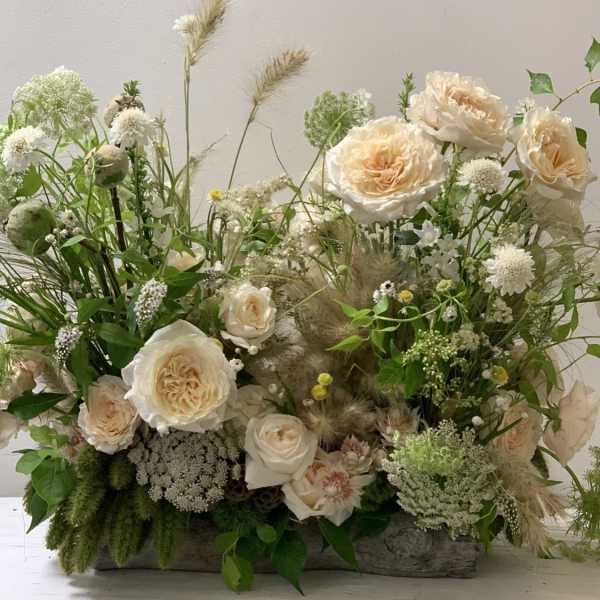 Cream roses and wildflowers arranged in a low rustic container