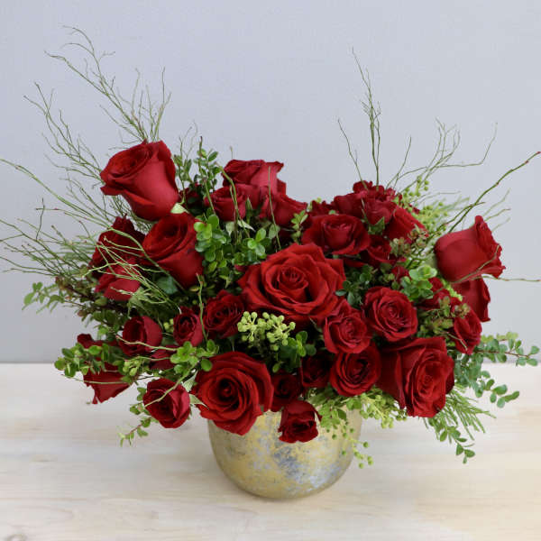Red roses arranged in a gold vase with airy greenery