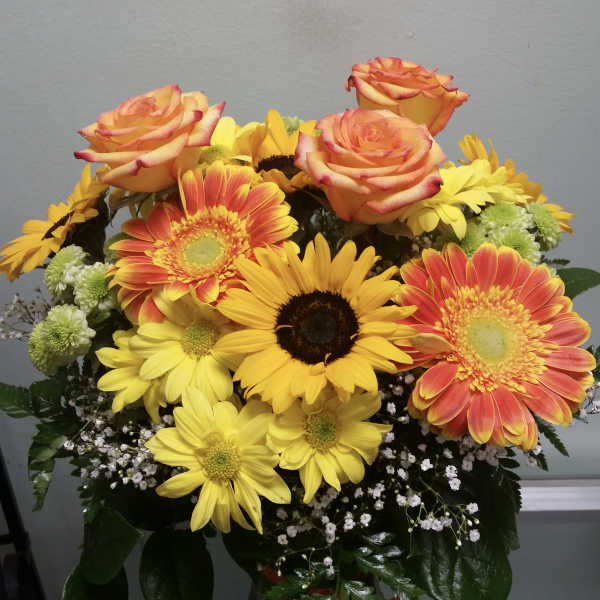 Bouquet of orange roses and yellow gerbera daisies in a glass vase