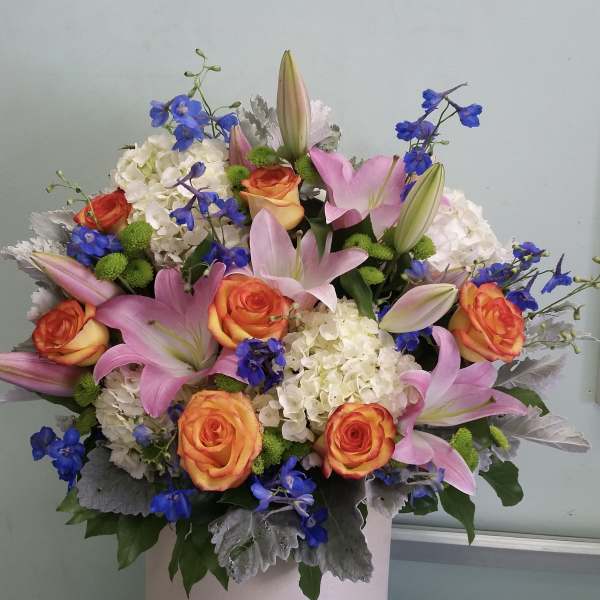 Bouquet of pink lilies, orange roses, and blue flowers in a pink hatbox