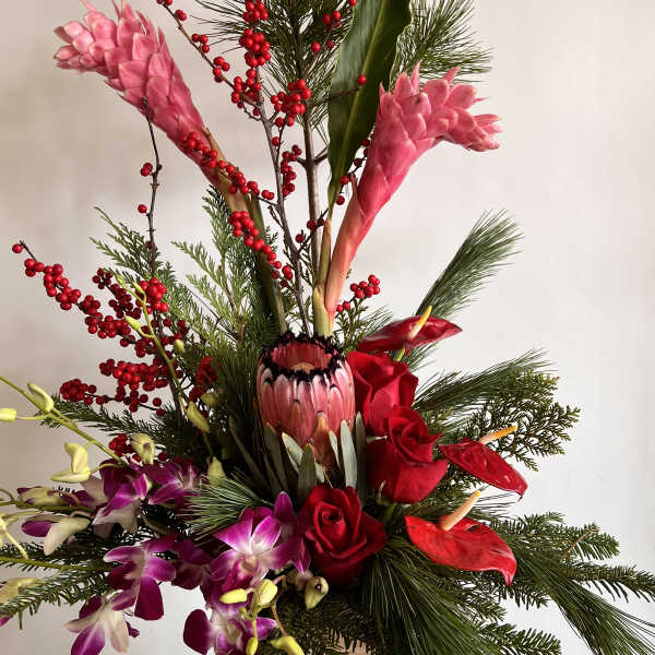 Tall tropical arrangement with pink ginger, red roses, and orchids in a wooden container