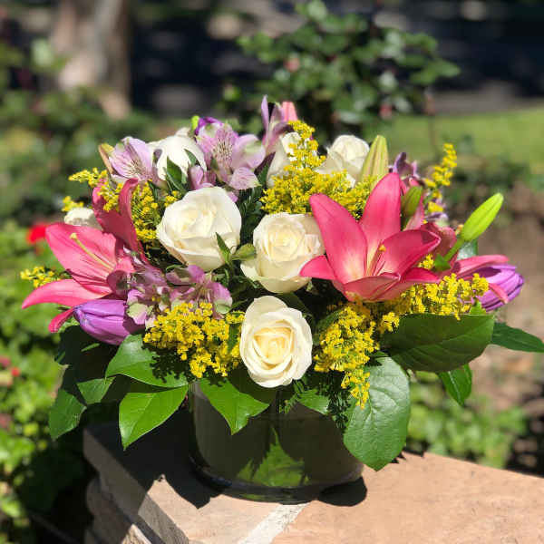 Bouquet of pink lilies, white roses, and yellow filler flowers in a dark vase