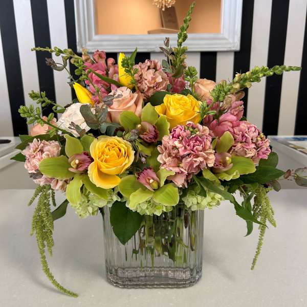 Mixed bouquet of yellow roses and pink flowers in a clear glass vase