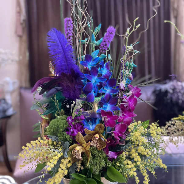 Tall arrangement of purple and blue orchids in a gold vase