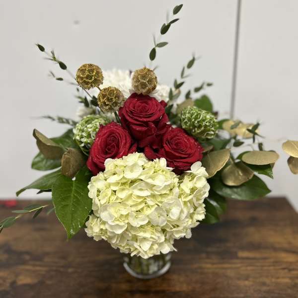 Red roses and white hydrangea in a glass vase with gold accents