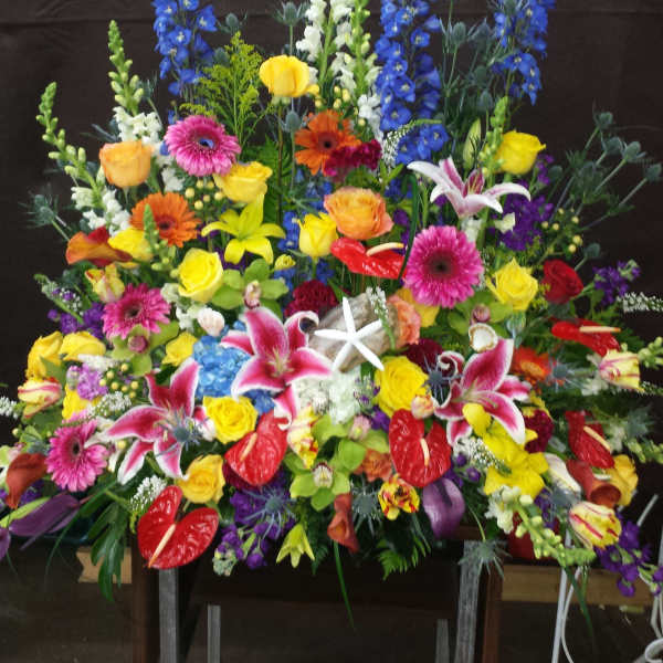 Large colorful funeral spray with lilies, roses, gerberas, and blue delphinium