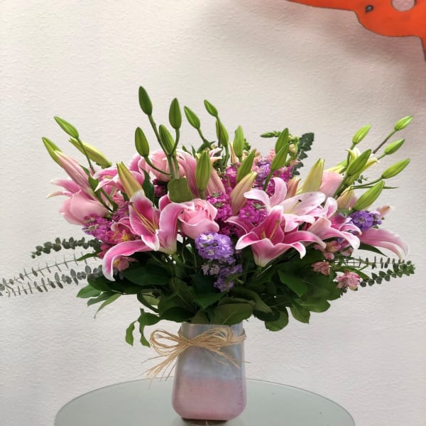 Pink lilies and purple flowers in a frosted vase with a bow