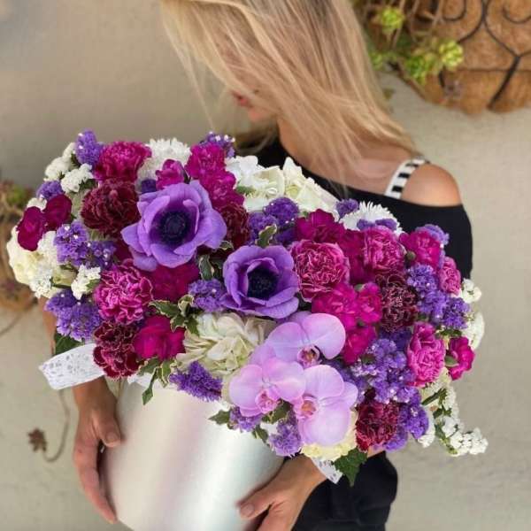 Woman holding a large purple, pink, and white flower arrangement in a white box