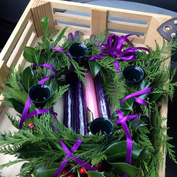 Evergreen wreath with purple ribbon and candle holders in a wooden crate
