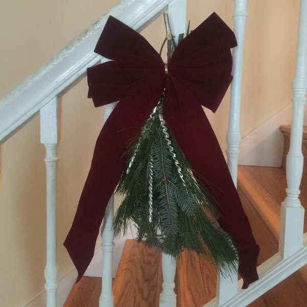 Holiday bow with evergreen sprigs hanging on a staircase railing