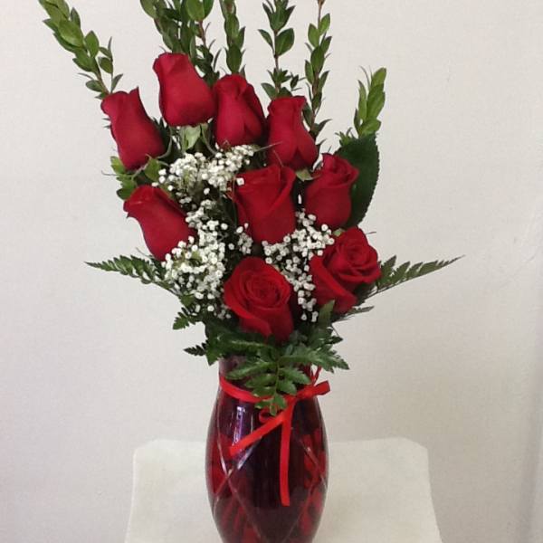 Red roses arranged in a red glass vase with baby's breath