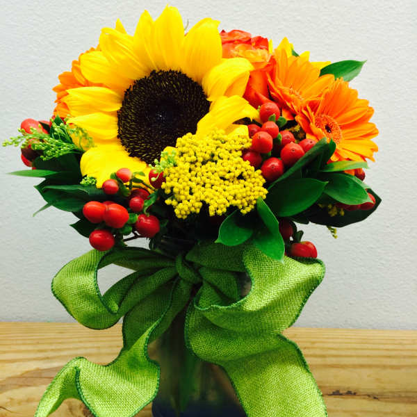 Sunflower and orange daisy bouquet in a glass vase with a green ribbon