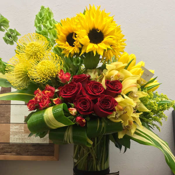 Bouquet of sunflowers, red roses, and yellow orchids in a tall glass vase