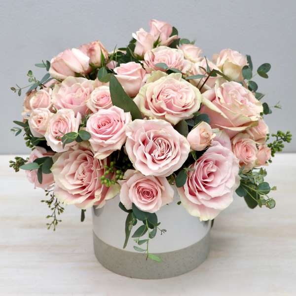 Low round arrangement of pale pink roses in a white cylindrical container