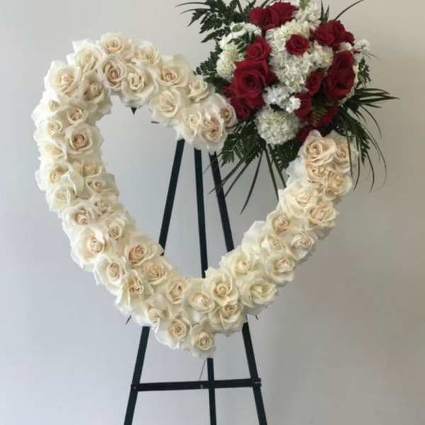 Heart-shaped floral wreath of white roses with a red rose cluster on an easel