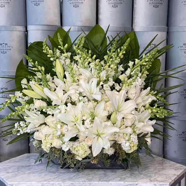 Large white floral arrangement with lilies and roses in a low container