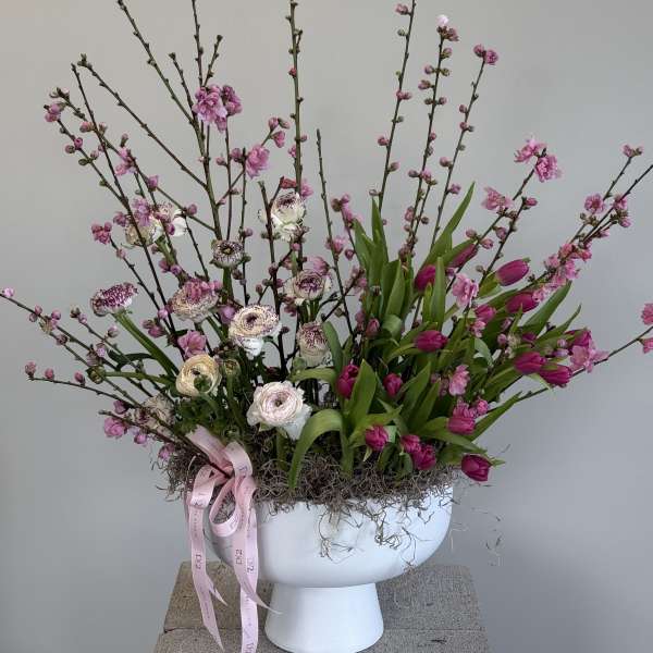 Pink blossoms and tulips in a white pedestal vase