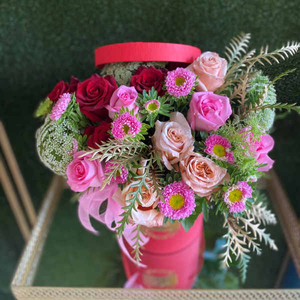 Bouquet of pink and red roses with small pink daisies in a pink hatbox