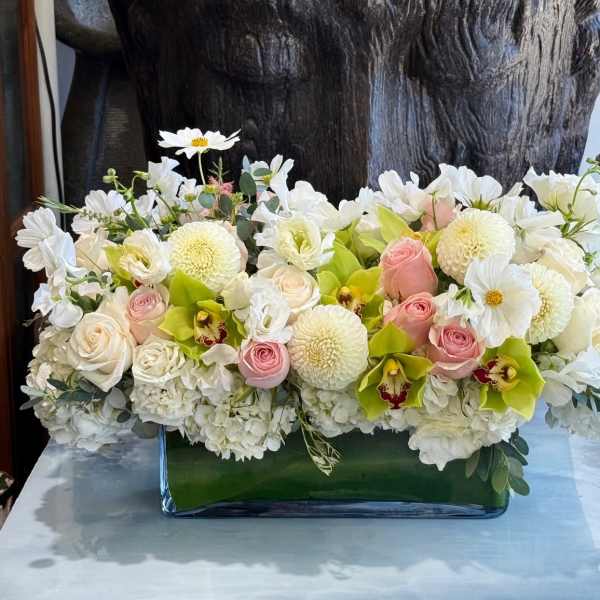 Low floral arrangement of white blooms, pink roses, and green orchids in a glass vase
