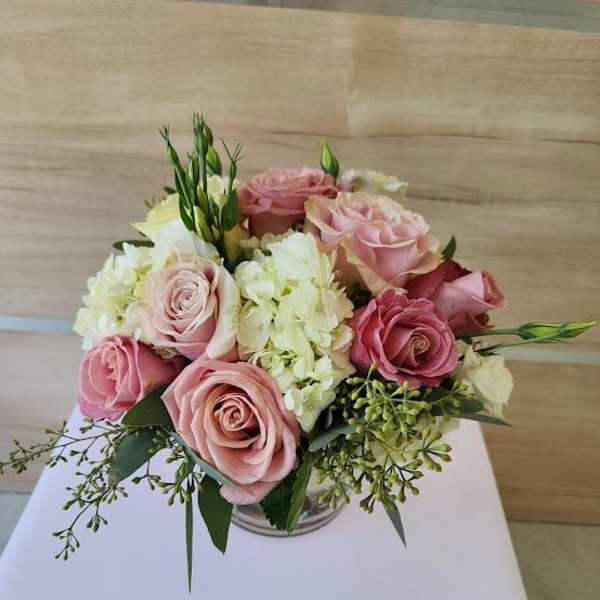 Low arrangement of pink roses and white hydrangeas in a clear glass vase