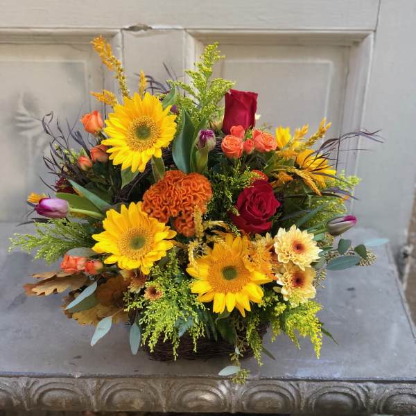 Mixed bouquet with sunflowers, red roses, and orange blooms in a basket
