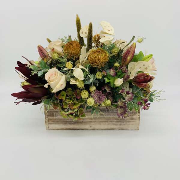 Low centerpiece of cream roses, golden protea, and mixed blooms in a rustic wooden box