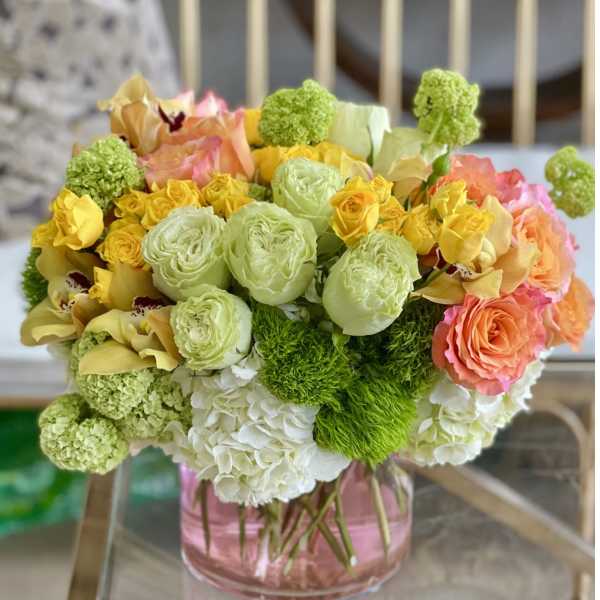 Bouquet of yellow, peach, and green flowers in a pink glass vase