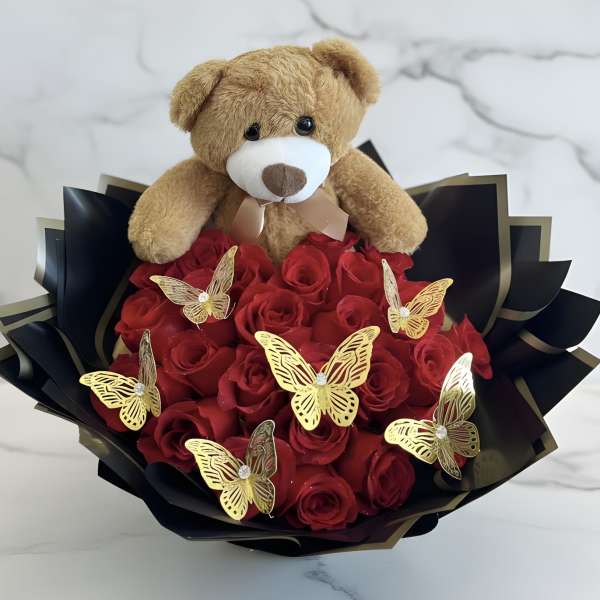 Teddy bear sitting on a bouquet of red roses with gold butterfly decorations