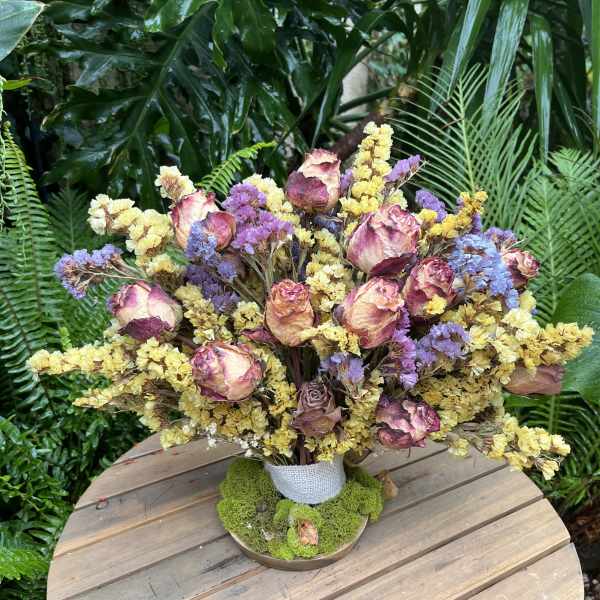 Dried roses and purple-yellow filler flowers in a wrapped vase arrangement