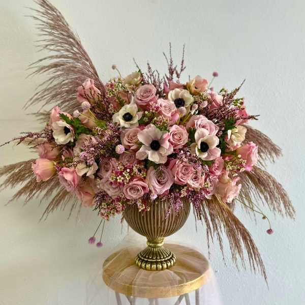 Pink rose and anemone arrangement in a gold vase with feathery pampas grass