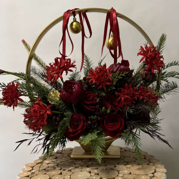 Red roses and holiday flowers arranged in a gold hoop with ribbon and ornaments