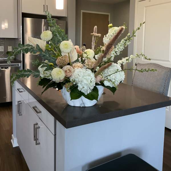 Large white floral arrangement in a marble-look bowl on a kitchen island